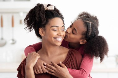 Sevimli siyah kız kahvaltıdan sonra güzel annesine sarılıp öpüyor. Mutfağın içinde. Afro-amerikan anne-kız kaynaşırken abur cubur yemek, kopyalama alanı