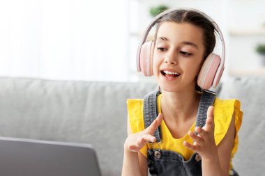 Kablosuz kulaklık takan genç bir kız internet konferansı yapıyor ve uzaktan öğretmeniyle internetten ders çalışıyor. Öğrenci web kamerasında konuşan dizüstü bilgisayar kullanarak uzaklık öğretmeniyle video sohbet öğrenme dersi alıyor