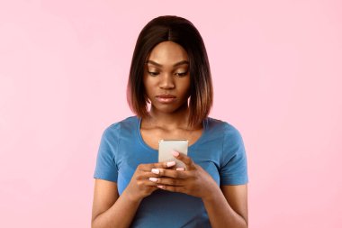 Ciddi Afrikalı Amerikalı Kadın Cep Telefonu Mesajlaşması ve İnternet Tarayıcısı Sarı Arkaplan 'ın üzerinde duruyor. Stüdyo Stüdyosu, memnun olmayan kadın akıllı telefonuyla poz veriyor. Mobil Uygulama Sayısı