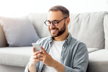 Mutlu milenyum adamı cep telefonu kullanıyor, oturma odasında oturuyor, çalışıyor ya da iletişim kuruyor, sosyal medyayı araştırıyor, evden bir arkadaşına ya da iş ortağına mesaj atıyor.