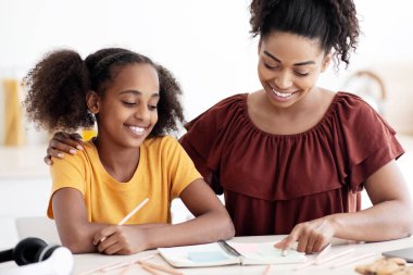 Yaratıcı siyahi anne ve kız okul projesinde birlikte çalışıyor, modern dizüstü bilgisayar kullanıyor, not alıyor, neşeli Afrikalı Amerikalı kadın genç çocuklara ödevlerinde yardım ediyor, mutfak içi, kopyalama alanı.