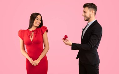 Düğün Teklifi. Erkek, kız arkadaşına evlenme teklif ediyor. Nişan yüzüğünü göstermek için elini uzatıyor. Sarı arka planda duruyor. Stüdyo Çekimi