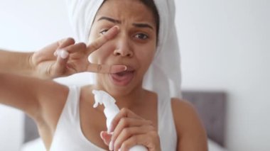 Kafasında havlu olan genç bir Afrikalı Amerikalı kadın evde elinde sprey şişesiyle cilt bakımının keyfini çıkarıyor.