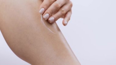 Genç bir kadın bacağına cilt bakımı ürünleri uyguluyor, kişisel bakım ve vücut şımartmayı vurguluyor. İzole edilmiş arka plan sağlıklı cilde odaklandığını vurguluyor..