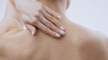 Genç bir kadın, sakin ve izole bir ortamda sırtına cilt bakımı ürünü sürmeye odaklanmış. Sahnede kendini şımartma ve vücut bakımı vurgulanıyor..