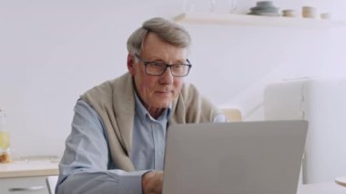 60 'lı yaşlarda yaşlı bir adam evinde rahat bir şekilde oturur ve dizüstü bilgisayarına odaklanır. Emeklilik hayatını seviyor, zihnini canlandıran aktivitelere katılıyor ve refahı arttırıyor..