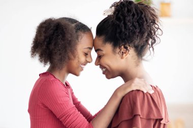 Birbirlerine sarılıp gülümseyen mutlu siyah anne ve kızın profil portresi, güzel Afro-Amerikan kadın anne ve genç kız mutfakta sarılıyorlar, fotokopi odası, yan görüş.