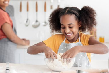 Güzel annesi bulaşık yıkarken, güzel siyah kız kurabiye için hamur topluyor. Afro-Amerikan kadın aşçı. Annesi kızına yemek yapmayı öğretiyor. Kıza odaklanıyor.