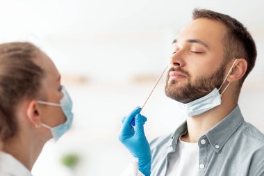 Klinikteki bin yıllık adam için burun koronavirüsü PCR testi yapan kadın doktor. Kafkasyalı genç bir adam teşhis prosedürü uyguluyor. Bulaşıcı hastalıkları koruma kavramı