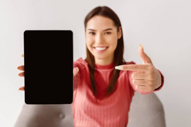 Mutlu beyaz kadın siyah boş ekranlı tableti işaret ediyor, yeni uygulama sunuyor, web sitesi için alan sunuyor, ürününüzün veya servisinizin reklamını yapıyor, seçici odaklanıyor