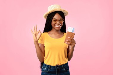 Yaz tatili. Mavi Stüdyo 'nun arka planında durup kameraya gülümseyen Şapka ve güneş gözlüğü takan Afro-Amerikan Kadın Seyahat Biletleri Tutuyor. Turizm ve Seyahat Konsepti