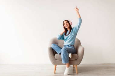 Kablosuz kulaklıklı neşeli genç beyaz bayan koltuğunda oturup müzik dinliyor, kolunu kaldırıyor, en sevdiği şarkıyla dans ediyor, popüler film müziğinin keyfini çıkarıyor, kopyalama alanının tadını çıkarıyor. Ev eğlenceleri