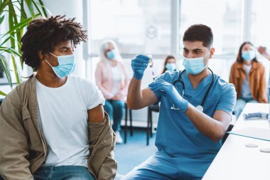Aşı ve bağışıklık sistemi. Doktor, hastaya iğne yapmadan önce şişeden ilaç alıyor. Genç adam tıp merkezinde grip ya da grip aşısı oluyor.