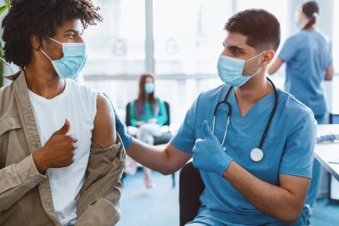 Afrika kökenli Amerikalı Adam ve Koruyucu Maske ve Eldiven Giyen Doktor Başparmaklarını kaldırarak Antiviral Coronavirus Aşısını Hastahanede alıyor. Corona Virüs Koruma, Tedavi ve İlaç