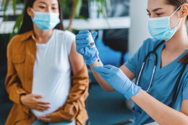 Coronavirus bağışıklığı. Şırıngayla gezen ve grip aşısı için ilaç alan mavi lateks eldiven ve koruyucu maske takan hamile bir kadın.