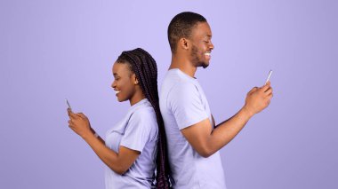 Modern yaşam tarzı. Sırt sırta duran, cep telefonlarını tutan ve internetten sohbet eden neşeli Afro-Amerikan çiftin profil yan görüntüsü, Violet stüdyo arka planı