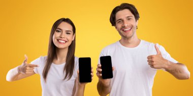 Bu uygulamayı seviyoruz. Elinde siyah ekranı olan iki akıllı telefonu elinde tutan ve gösteren mutlu bir çiftin portresi. Cihazı gösteren genç bayan, işaret parmağı gösteren adam, panorama.
