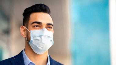 Medikal maske takan orta doğulu bir işadamı ve resmi kıyafet ofis binasının yanında duruyor, fotokopi alanına bakıyor, yakın plan portresi çekiyor. COVID-19 salgın konsepti