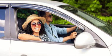 Yazlık şapkalı, güneş gözlüklü, gülümseyen genç bayan kameraya bakıyor. Sevgilisiyle araba gezisine çıkıyor. Orta doğulu çift birlikte tatile çıkıyor.