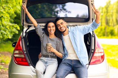 Duygusal ortadoğulu çift kırsal bölgede kahve içiyor, açık bir araba bagajında oturuyor, kucaklaşıyor ve el kol hareketi yapıyor, araba gezintisi yaparken kahve molası veriyor, tatilin tadını çıkarıyor, fotokopi çekiyor.