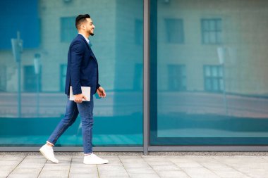 Caddede yürüyen neşeli genç Arap işadamı başarılı bir ortadoğu girişimcisi veya CEO 'su iş toplantısı yapıyor dijital tablet, ofis binası geçmişi, kopyalama alanı.