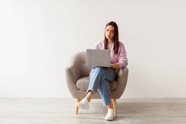 Beyaz stüdyo duvarına dizüstü bilgisayarla oturmuş gülümseyen beyaz kadın, kopyalama alanı. Odaklanmış milenyum hanımı taşınabilir bilgisayarla çalışıyor ya da çalışıyor.