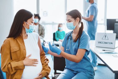 Aşı, bağışıklık sistemi, Hastalık Önleme Konsepti. Hastanede grip ya da grip aşısı olan maskeli hamile bir kadın. Profesyonel hemşire ya da doktor hastaya antiviral iğne yapıyor.