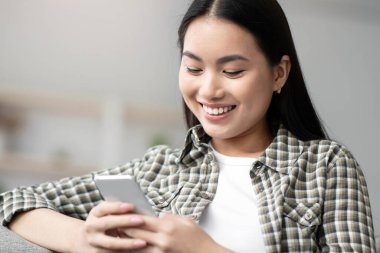 Kanepede oturan neşeli Asyalı kadın akıllı telefon kullanıyor, kız arkadaşı ya da sevgilisiyle sohbet ediyor, fotokopi çekiyor. Cep telefonlu güzel genç bir kadın kanepede dinleniyor, sosyal medyayı kontrol ediyor, kapatıyor.