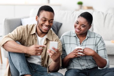 Afrika kökenli Amerikalı turistler, seyahat başvurusu için telefon kullanıyor. Online Planlama Biletleri. Siyah Eşler İçerideki Bavulun Yanında Oturan Akıllı Telefon 'da İnternet' e Bakıyorlar