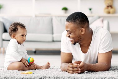 Genç, mutlu, Afrikalı bir babanın evde tatlı bir bebekle oynadığı, siyahi bir babanın sevimli küçük bir çocuğa baktığı, gülümsediği, babalığının tadını çıkardığı, boşluğu kopyaladığı portresi.