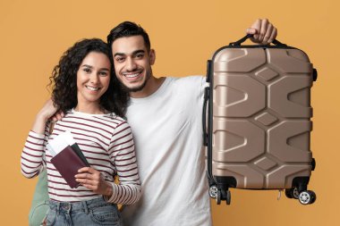 Aile gezisi. Pasaportlu ve çantalı mutlu bir Arap çift sarı arka planda poz veriyor, neşeli Orta Doğu eşleri bavullarını ve biletlerini tutuyor, seyahat için hazır, kopyalama alanı