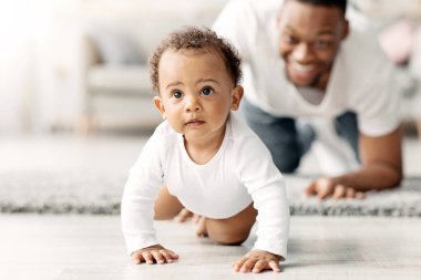 Mutlu siyah baba evde yerde sürünen sevimli bebeğe bakıyor, gururlu Afrikalı Amerikalı baba tatlı çocuğuyla vakit geçiriyor, babalık izninin tadını çıkarıyor, seçici bir şekilde odaklanıyor.