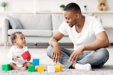 Siyah milenyum babası ve sevimli bebeği evlerinde bina bloklarıyla oynuyorlar, Afrikalı genç babası tatlı çocuğuyla birlikte oturma odasında otururken eğleniyorlar.