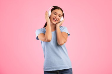 Bu melodiyi seviyorum. Kapalı gözlerle müzikten hoşlanan, kablosuz kulaklıklara dokunan, dans eden, dinlenen ve sarı stüdyo duvarından izole edilmiş favori şarkıyı dinleyen pozitif kaygısız kadının portresi.