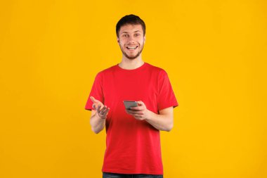 Harika bir uygulama. Akıllı telefon kullanan ve mavi stüdyo arka planında izole edilmiş pozlar veren heyecanlı duygusal bir adamın portresi. Gülümseyen adam kameraya bakıyor, elinde aletle.