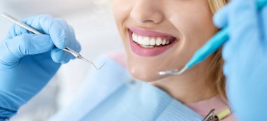 Dişçi muayenehanesinde tedavi görürken güzel beyaz dişlerini gösteren kadın hastaya yakından bakın. Diş aletleri, panorama gibi plastik eldivenler tutan dişçi elleri. Düzenli check-up yaptıran kadın
