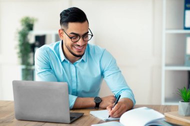 Modern ofisteki online iş toplantısı sırasında bilgi yazan Arap girişimci. Milenyum işadamı not alıyor, eğitici webinar izliyor, konferansa katılıyor.