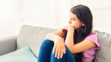 Stresli Hintli genç kız evdeki kanepede oturuyor, yan tarafa bakıyor, üzgün ve yalnız hissediyor, kapalı kapılar ardında iletişim eksikliğinden muzdarip. Gençlik depresyonu konsepti