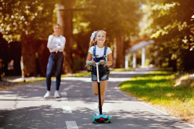 Scooter 'a binen küçük kız hafta sonunu annesiyle şehir parkında geçiriyor. Yaz etkinliği konsepti. Seçici Odaklanma