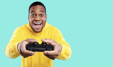Heyecanlı Afrikalı Amerikalı Oyuncu Oyun Oynayan Oyun Arkadaşı Mavi Stüdyo Arkaplanı Üzerinde Joystick Oynuyor, Kameraya Gülümsüyor. Oyun Konsepti. Yeni Video Oyunu Reklamı