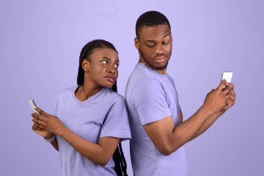 Mahremiyet, Güvensizlik, Sadakatsizlik. Meraklı siyah adam kız arkadaşlarına bakmaya çalışıyor akıllı telefon, kafası karışmış kadın cihazını saklıyor, mor stüdyo arka planında duran çift.