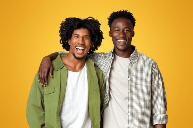 Erkek Arkadaşlığı Konsepti. Kameraya sarılıp gülümseyen iki mutlu siyahın portresi, Milenyum Afrikalı Amerikalı eşlerin bej rengi stüdyo arka planında poz verirken eğlenmesidir.