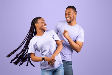 Hayatın tadını çıkarıyorum. Mutlu Afrikalı Afrikalı Amerikalı partnerlerin portresi dans ediyor ve eğleniyor, birbirine bakıyor, pastel mor menekşe renkli stüdyo arka planında izole edilmiş, boşluğu kopyalıyor