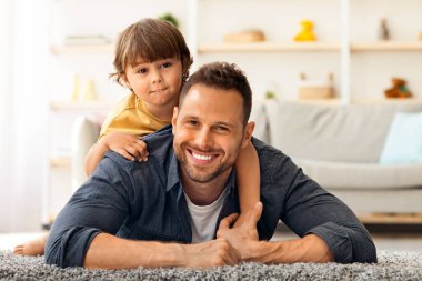 Mutlu erkek nesiller. İçerde, neşeli genç babasının ve küçük tatlı oğlunun, kameraya gülümseyen, evde yerde yan yana uzanmış, boş bir alan portresi.