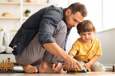 Sevgi dolu baba ve oğul ahşap tren oyunu oynuyorlar. Hafta sonunu birlikte geçiriyorlar. Sevecen baba ve tatlı çocuk sıcak zeminde oturuyorlar.