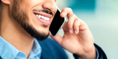 Açık havada duran, cep telefonuyla konuşan, iş ortağıyla iyi haberler paylaşan resmi takım elbiseli Arap işadamı.