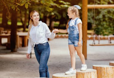 Neşeli anne ve küçük kızı şehir parkında modern oyun alanında el ele tutuşuyorlar. Ana Konseptle Hafta Sonu