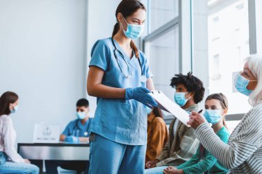 Coronavirus Tedavisi ve Aşı. Hastane bekleme odasında Doktor 'la Maskeli Kadın İmza Evrakları. Corona Virüs Bağışçılarından Plazma Bağışları, Grip Salgını Tıbbi Konsepti
