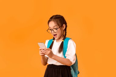 Mobil Oyunlar. Heyecanlı Asyalı Okul Çocuğu Stüdyoda Sarı Arkaplan Üzerine Akıllı Telefon Poz Veriyor.