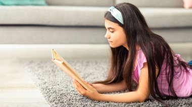 Ev eğlencesi konseptini bozma. Zeki Hintli genç kız ilginç bir kitap okuyor, oturma odasında yerde yatıyor. Zeki ergen hikayeden zevk alıyor, sınava ya da sınava içeride çalışıyor.